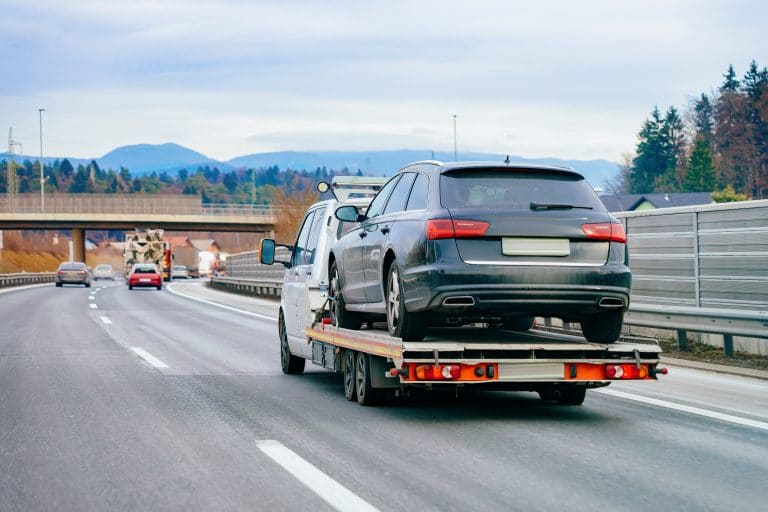 Ein Abschleppwagen transportiert eine schwarze Limousine auf einer Autobahn, repräsentativ für die Dienste von Autoankauf Online im Fahrzeugtransport und Handel.